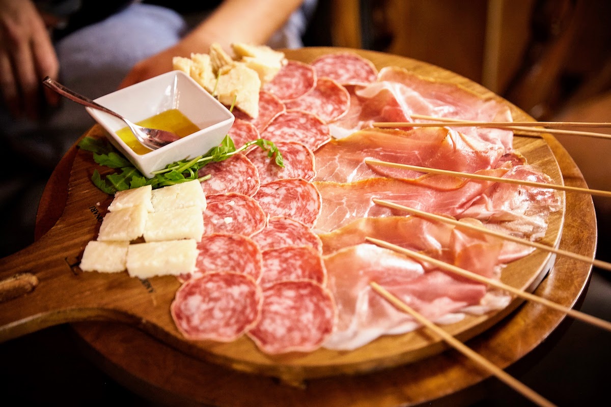 Close up of an Italian charcuterie board with slices of prosciutto, salami, various cheeses, and a small dish of honey.