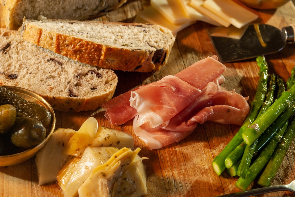 Prosciutto, olives, asparagus, cheese, and bread on a wooden serving board