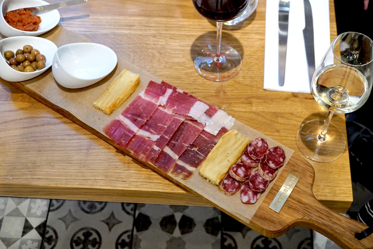Charcuterie and cheese displayed on a wooden board beside two glasses of wine