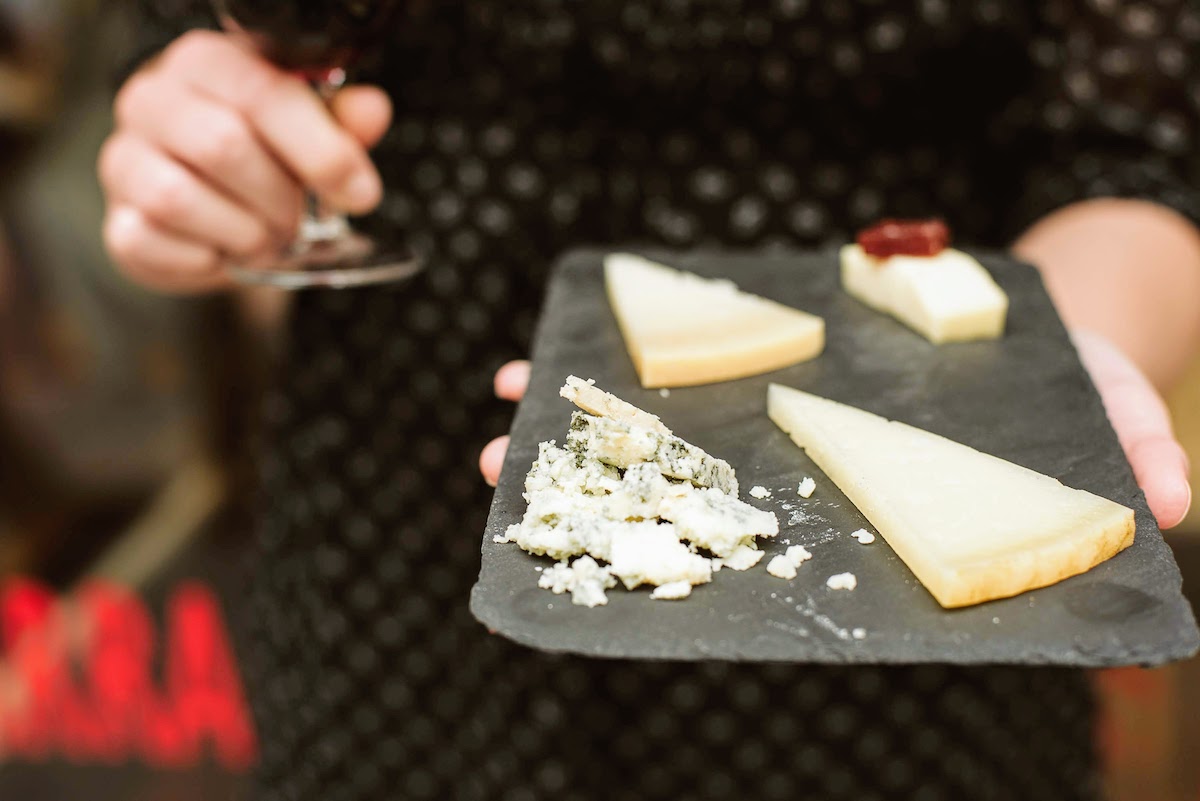 Close up of a person holding a small black tray with 4 different cheeses