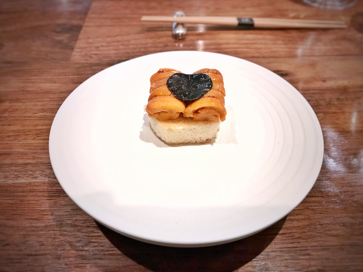 Hokkaido uni, black truffle, and brioche served on a white plate.