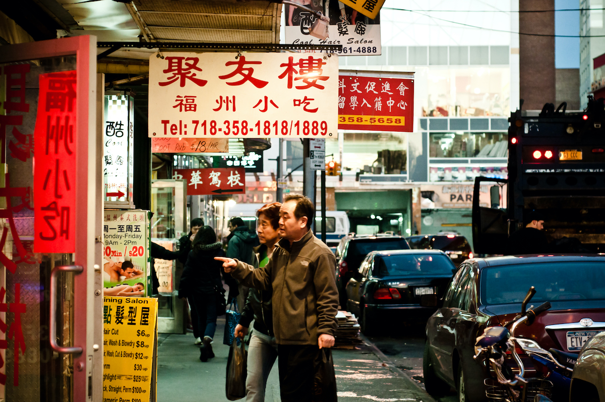 A Chinese couple looking at signs outside a storefront in Chinatown, Queens