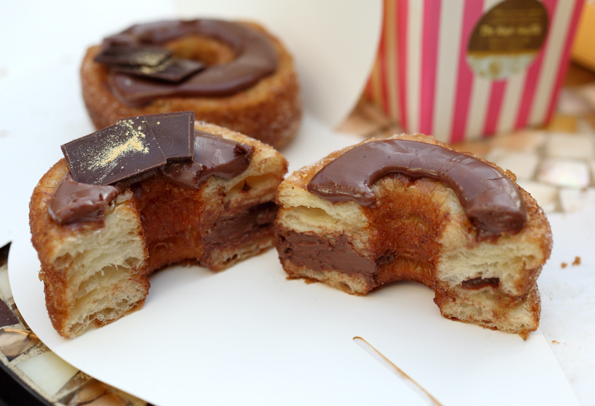 One whole chocolate cronut and one sliced in half on a white surface