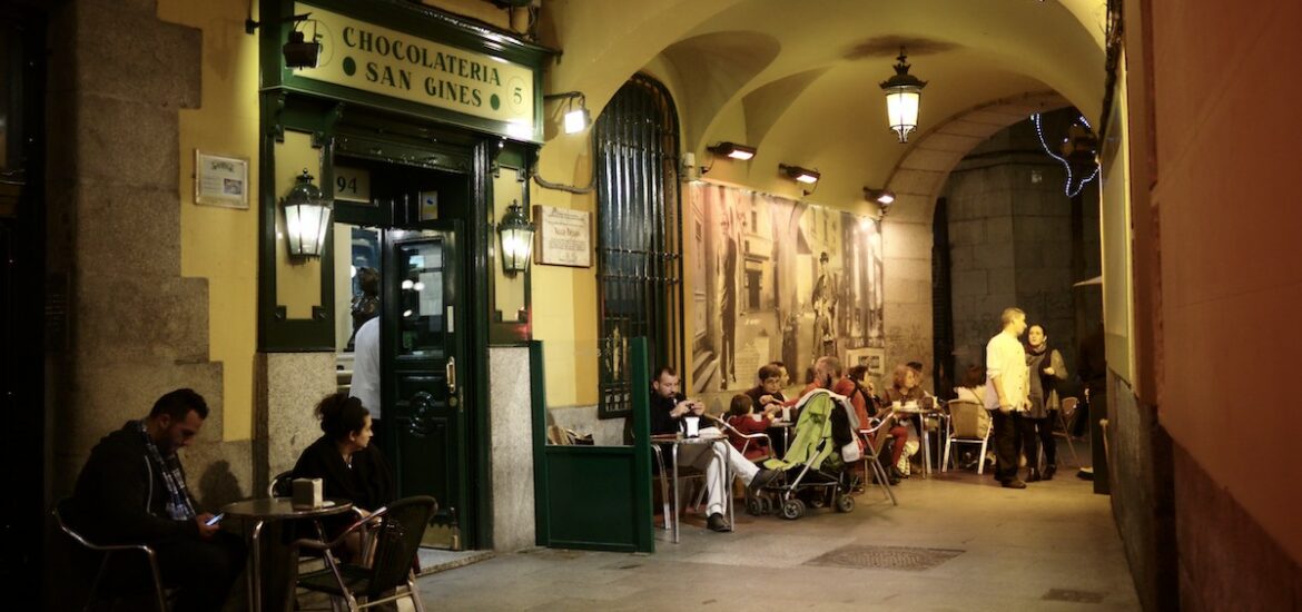 Exterior of a cafe in an arched passageway with people sitting at the terrace tables.
