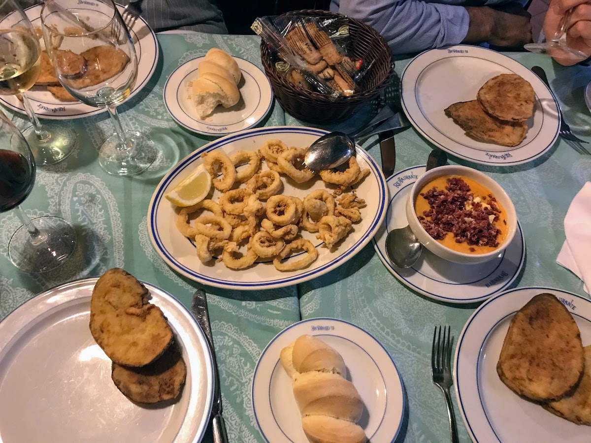 Overhead shot of a table with multiple plates of tapas-style dishes and glasses of wine.