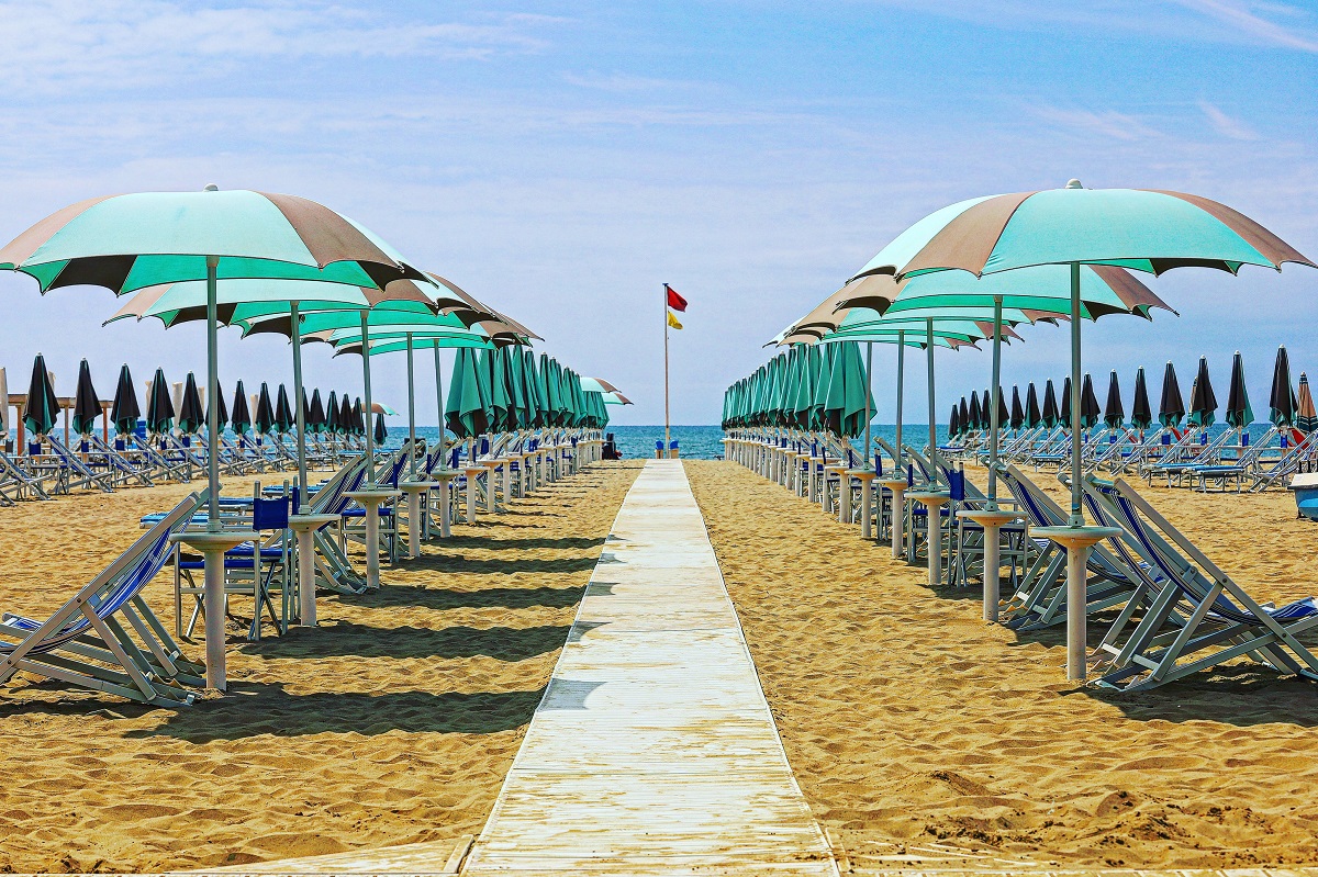 Sandy beach filled with beach chairs with umbrella and a pathway leading to the water