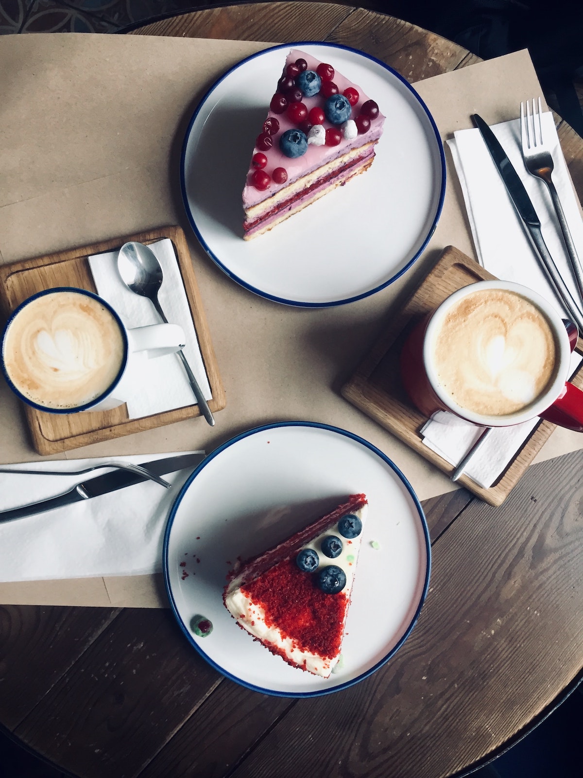 Overhead shot of two slices of cake with berries on white plates and two lattes.