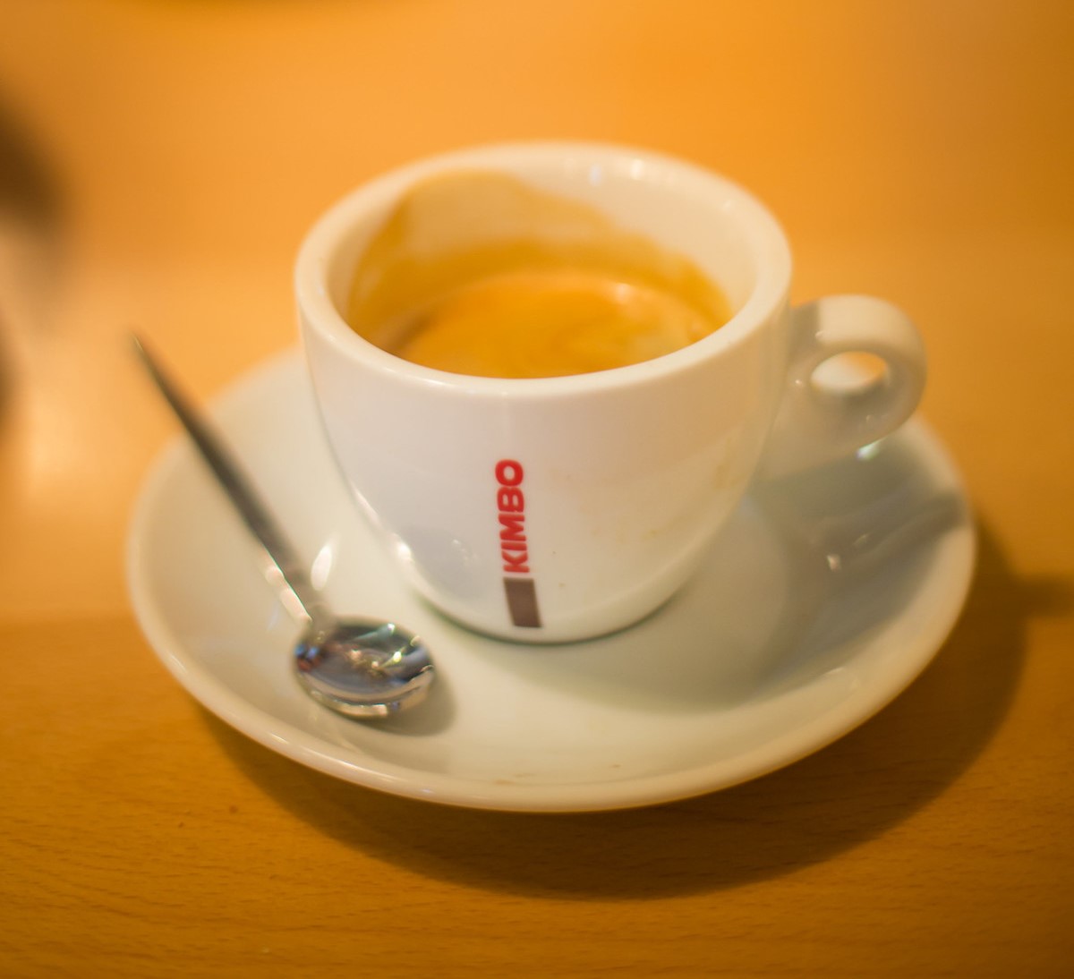 close up of a small white espresso cup with read letters on the side reading "Kimbo," a common coffee roaster found in Naples