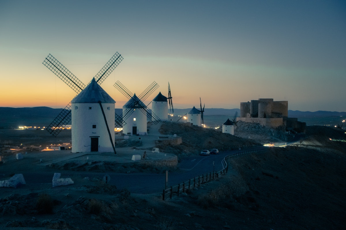 Sunset view of five large white windmills with a stone castle in the background.