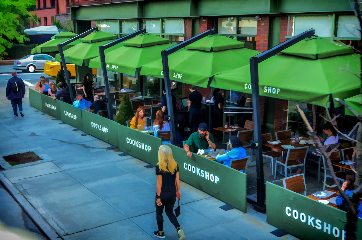 Outdoor dining terrace at Cookshop in NYC with tables set up under green umbrellas