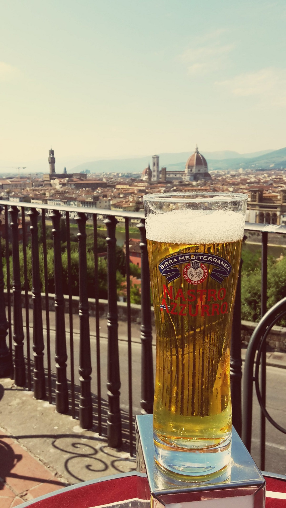 A long, tall glass of pale beer in the foreground with the Florence duomo in the background