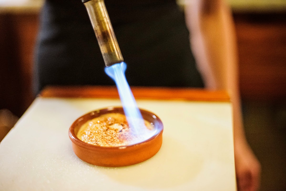 A dessert similar to creme brulee in a small clay dish being caramelized with a blowtorch