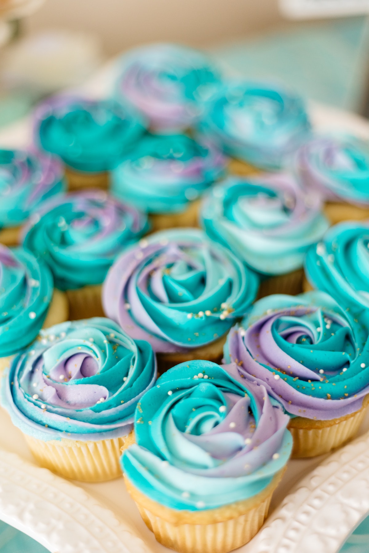 Tray of white cupcakes decorated with purple and blue frosting.