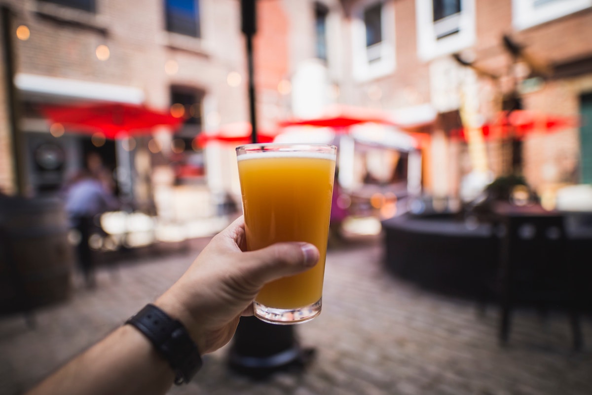 close up of someone's hand holding a glass of beer with a blurry plaza in the background