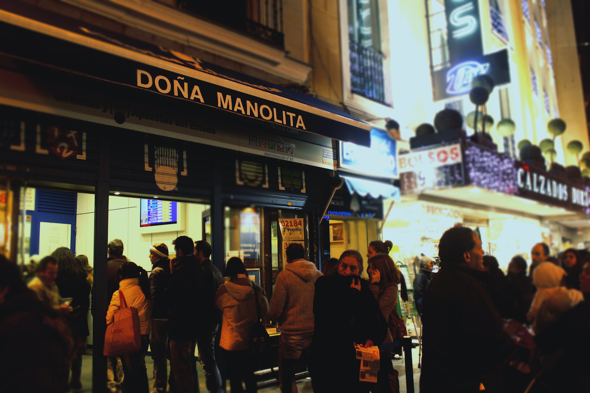 People lining up at a lottery ticket booth under an awning reading Doña Manolita