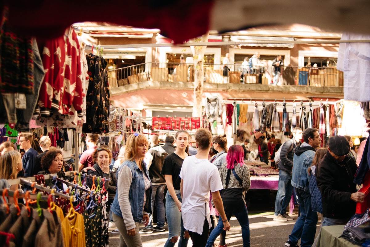 Crowd of people walking by clothing stalls at a flea market.