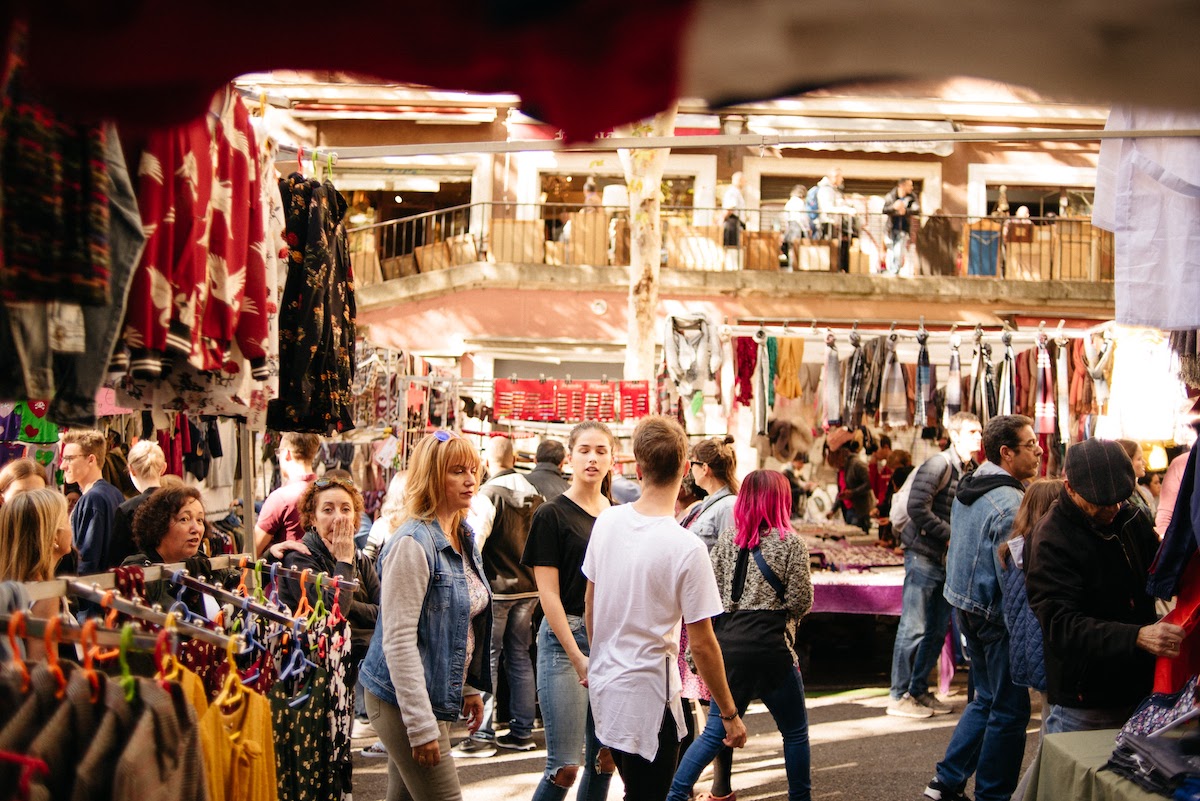 Crowd of people walking by clothing stalls at a flea market shopping in Madrid.