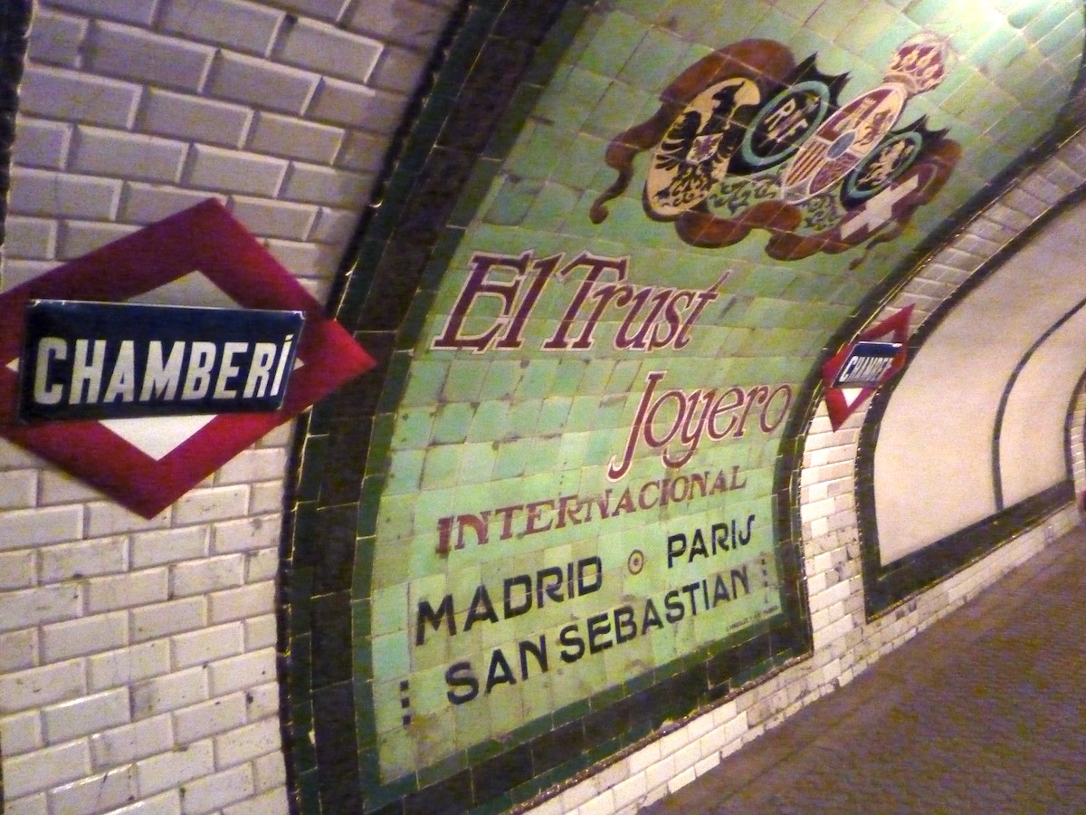 Colorful vintage advertisement with a green background laid into the tiles of an old subway station.