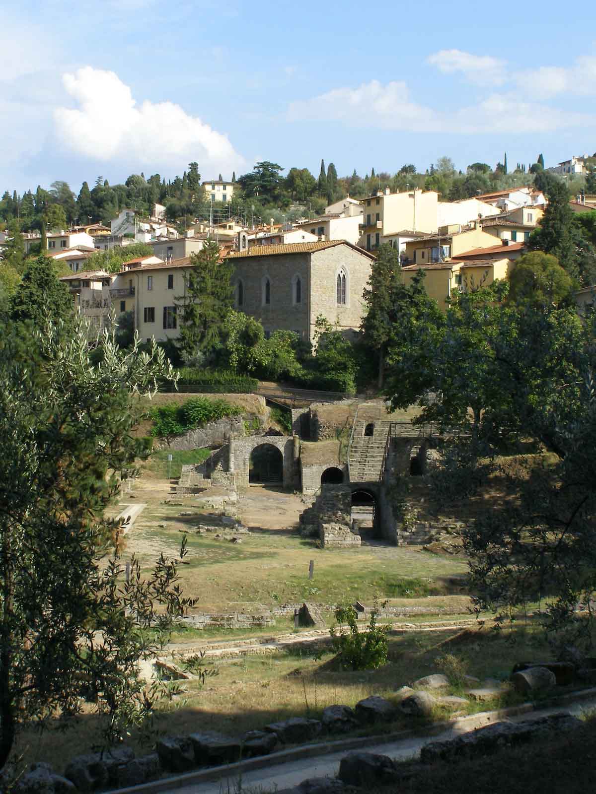 Tuscan town with ancient ruins in the foreground and more modern buildings in the background.