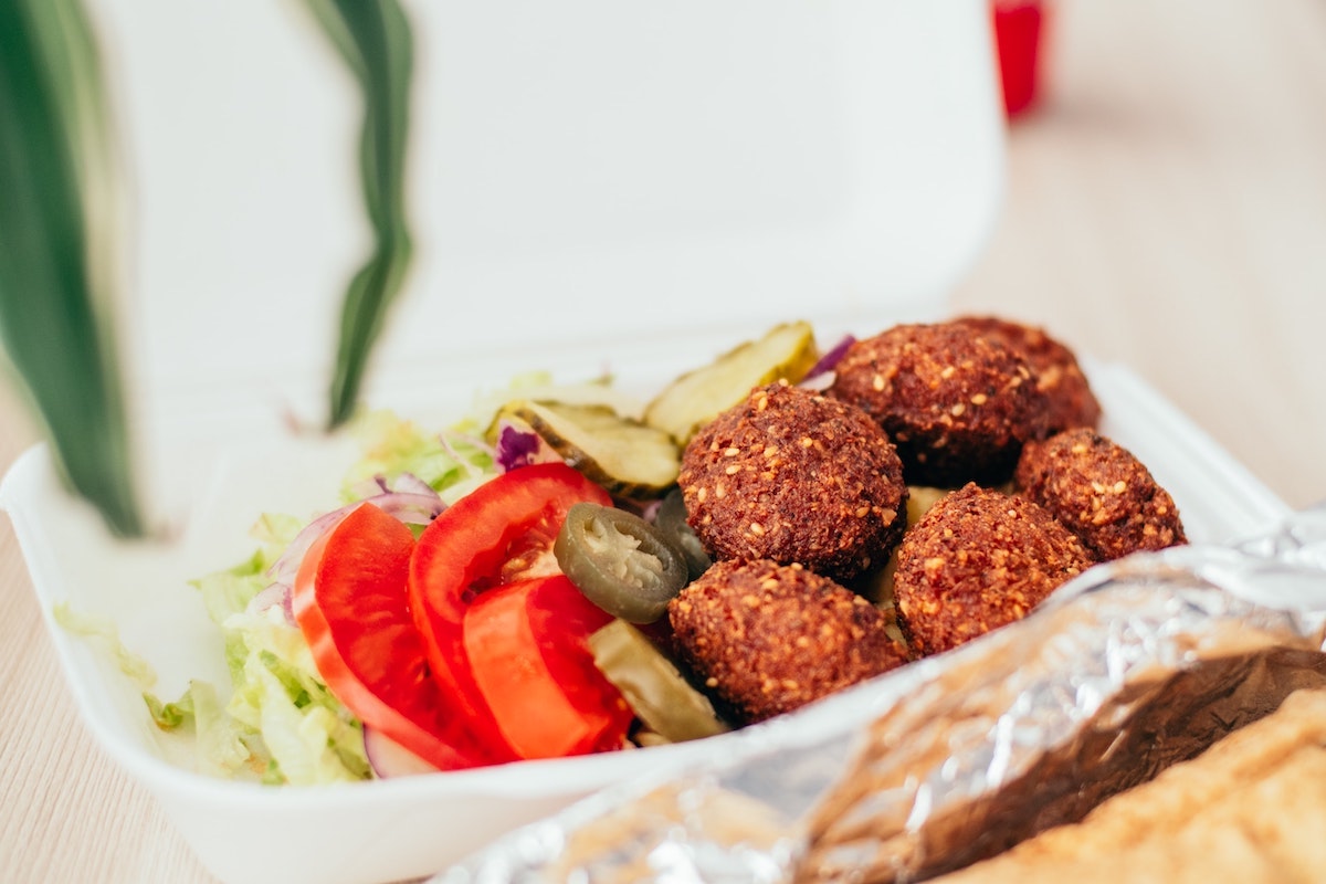 Falafel balls, lettuce, pickles, onions, and jalapeños in a styrofoam dish