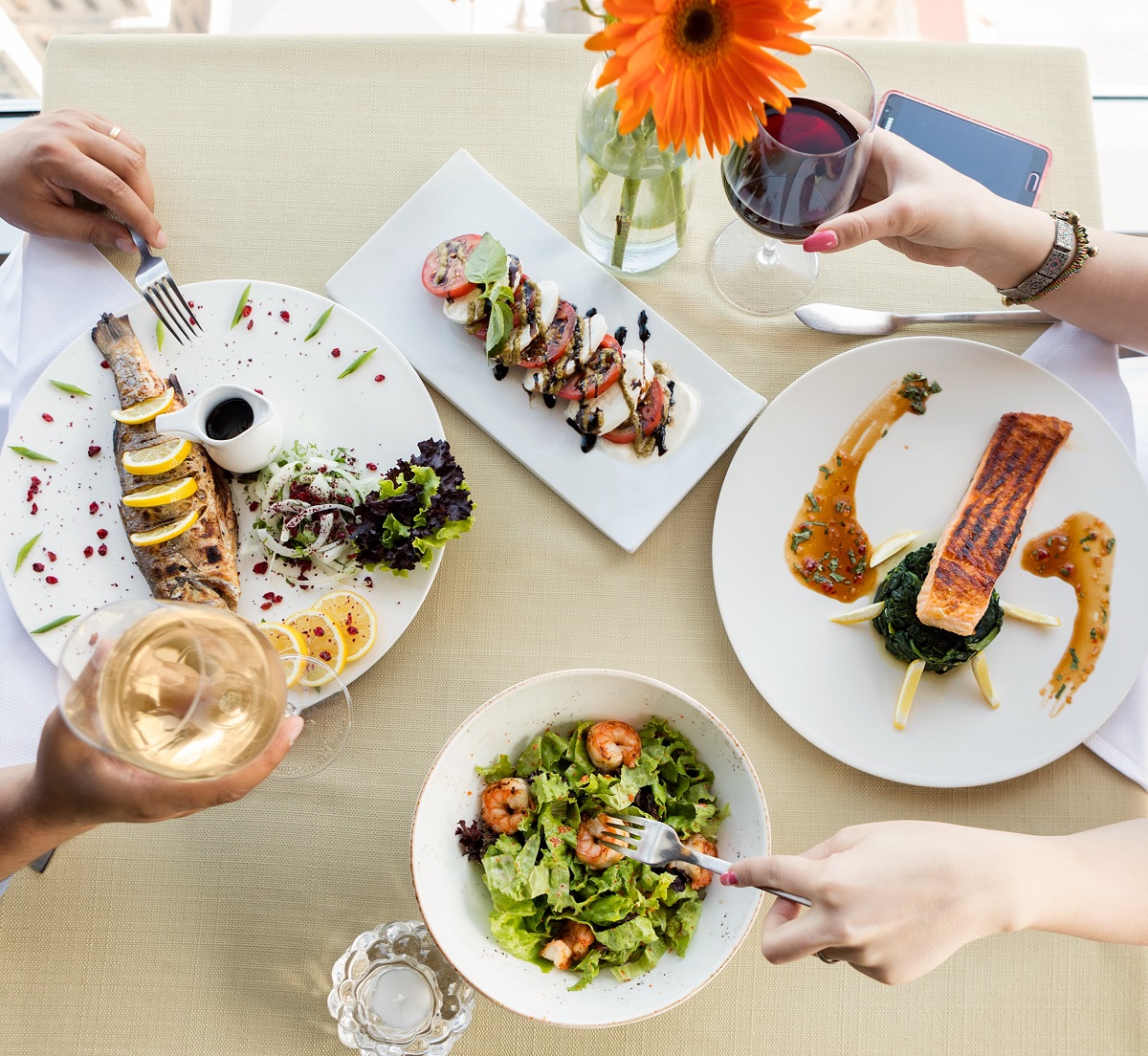 Couple sharing a restaurant meal with many small dishes including salad with shrimp, grilled fish, salmon, and sliced tomatoes