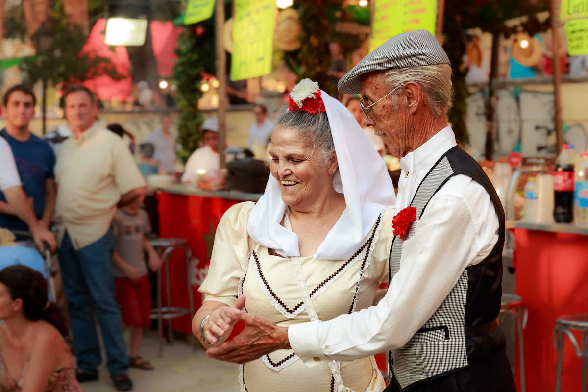 Older couple in traditional dress from Madrid, Spain smiling as they dance together.