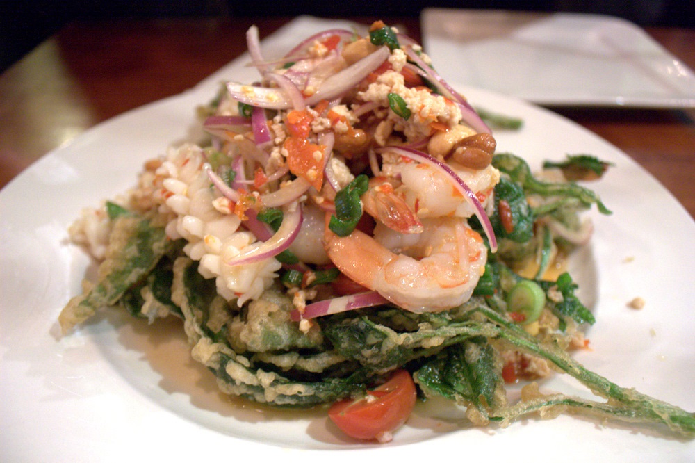 Green salad with fried greens, seafood, shrimp, and red onions on a white plate