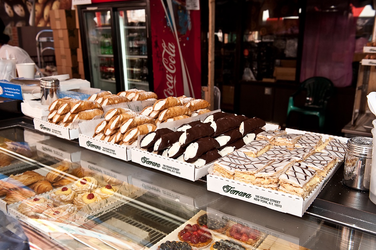 Trays of chocolate canoli and cream-filled pastries on top of an outdoor counter
