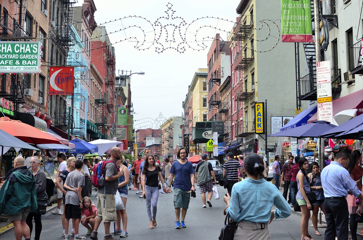 A couple strolls down a busy street in NYC surrounded by street lights, stores, and other pedestrians