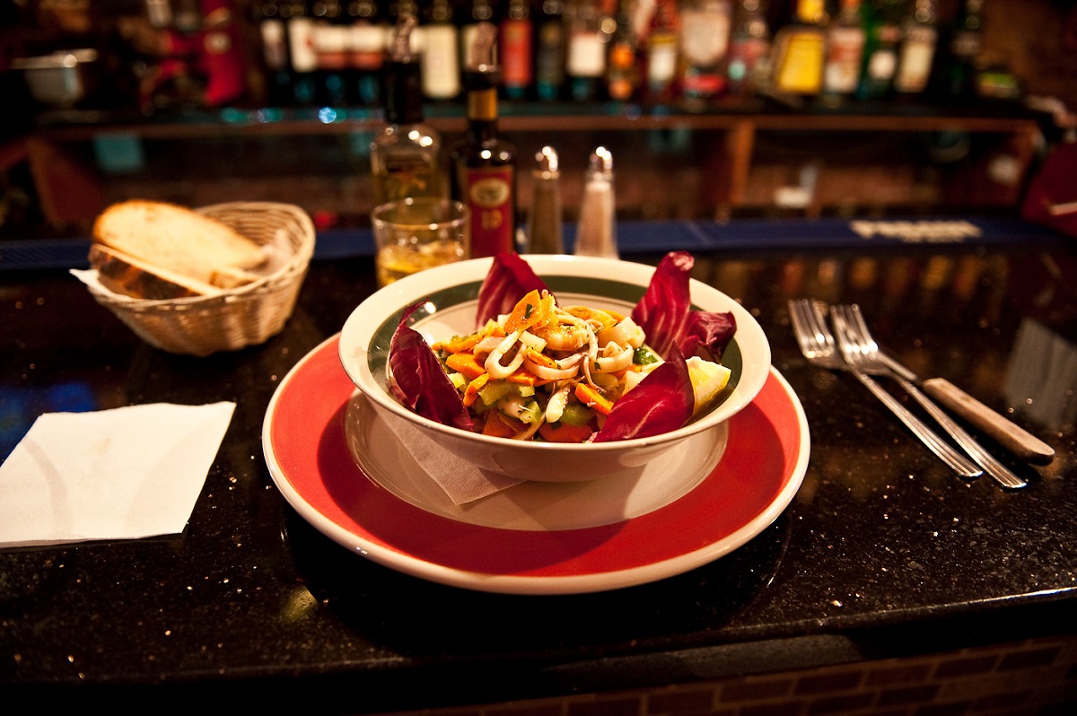 Fancy bowl of salad topped with seafood on top of a black marble counter