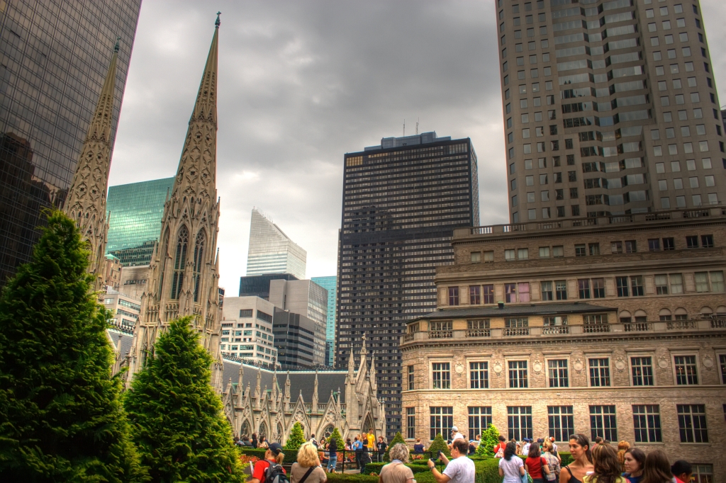 Rooftop garden with tourists beside a cathedral and city skyline