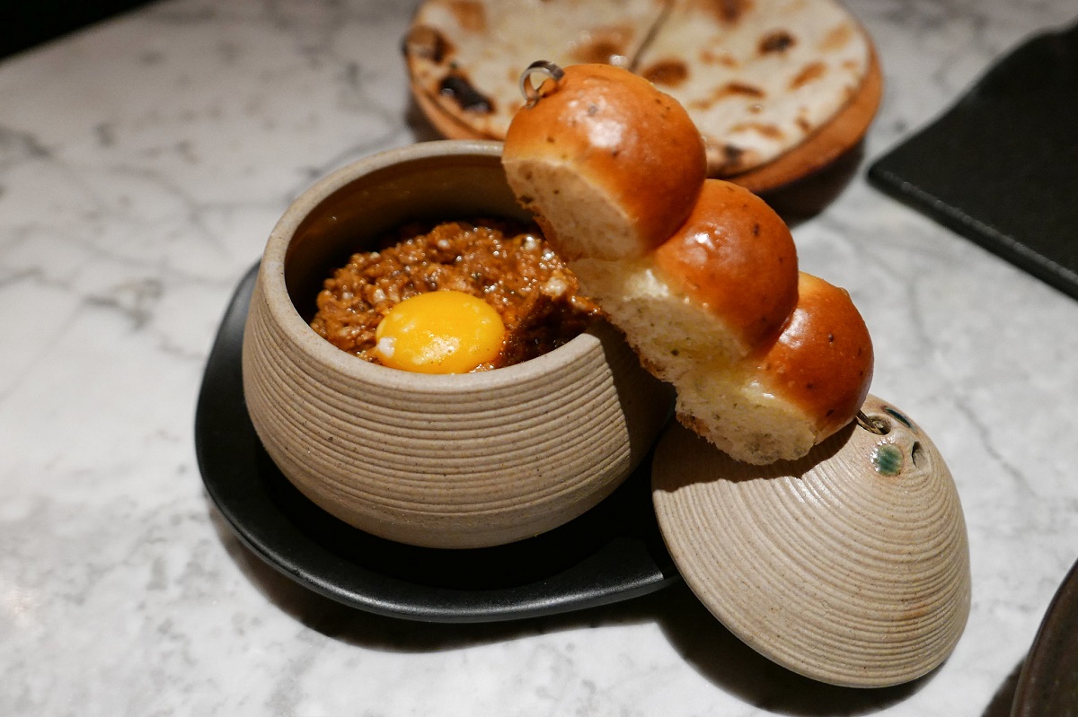 Smal cylindrical bowl with Indian food topped with an egg and served with skewered buns