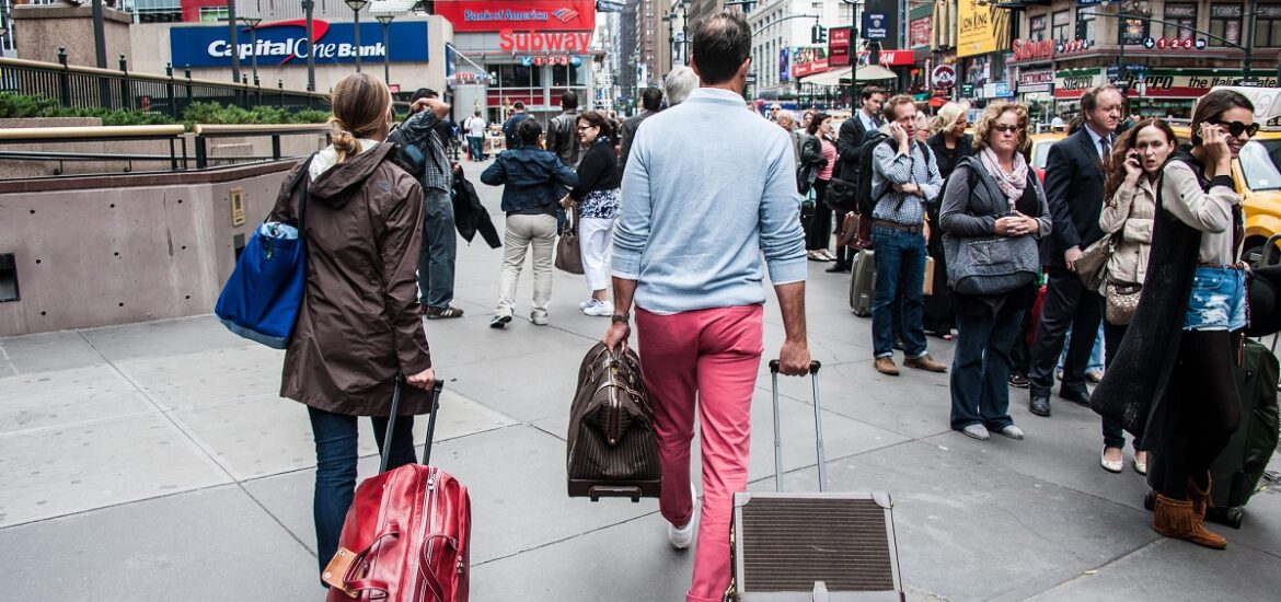 Couple walks down a busy street carrying suitcases