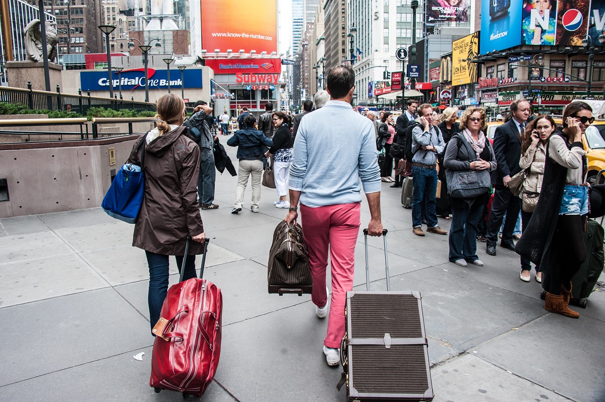 Couple walks down a busy street carrying suitcases