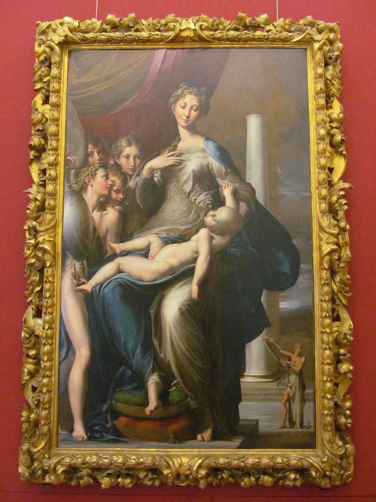 An oil painting in a golden frame of a woman with a long neck holding a strangely large baby
