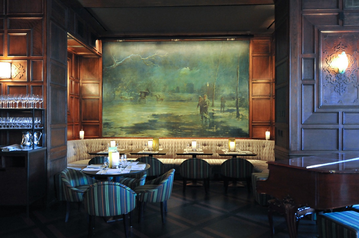 Wood paneled bar and restaurant with dining tables with a large painting on the wall