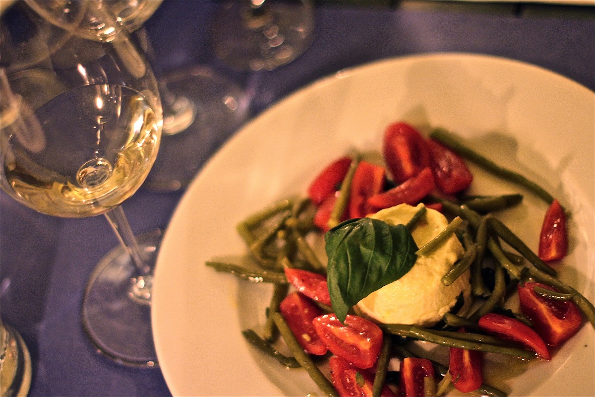 Dish of green beans, tiny tomatoes and burrata with a glass of white wine