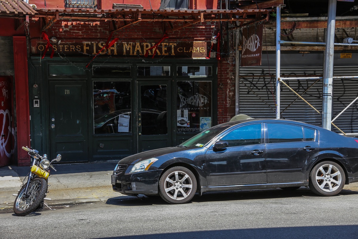 A car parked under scaffolding outside of a restaurant that reads "fish market"