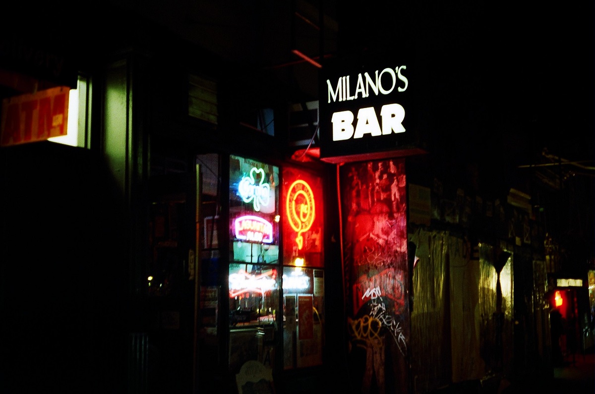 White neon sign outside of a quiet city street that reads "Milano's Bar"