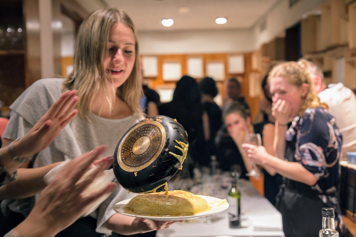 A woman flipping a Spanish omelet out of a pan onto a plate while several people watch