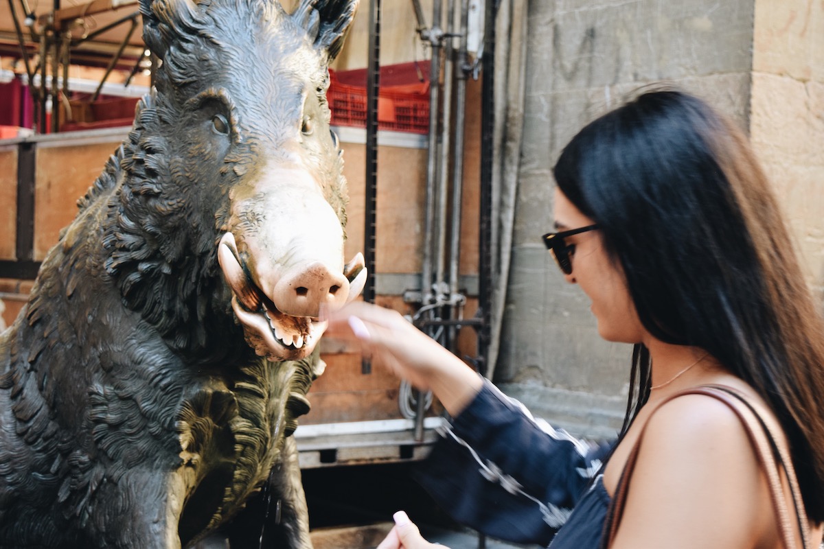 Woman rubbing the nose of a boar statue