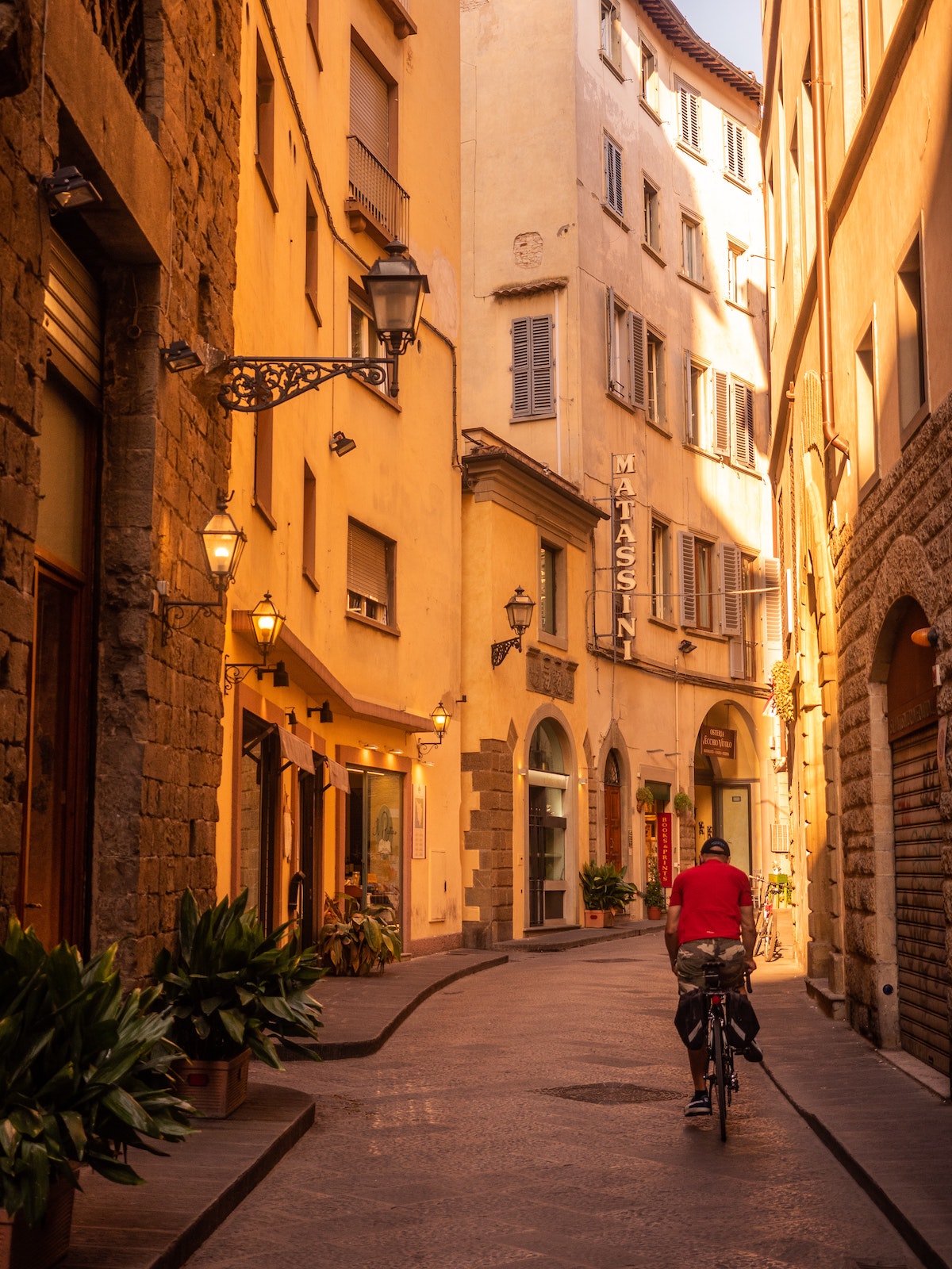 A person in a red jacket riding a bike on a pedestrian street in Florence
