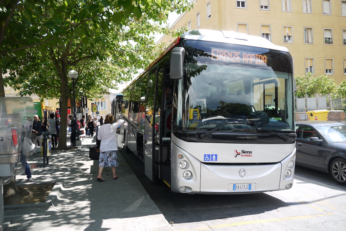 People boarding a bus in Siena, Italy with the screen above the front window reading "Firenze Rapida."