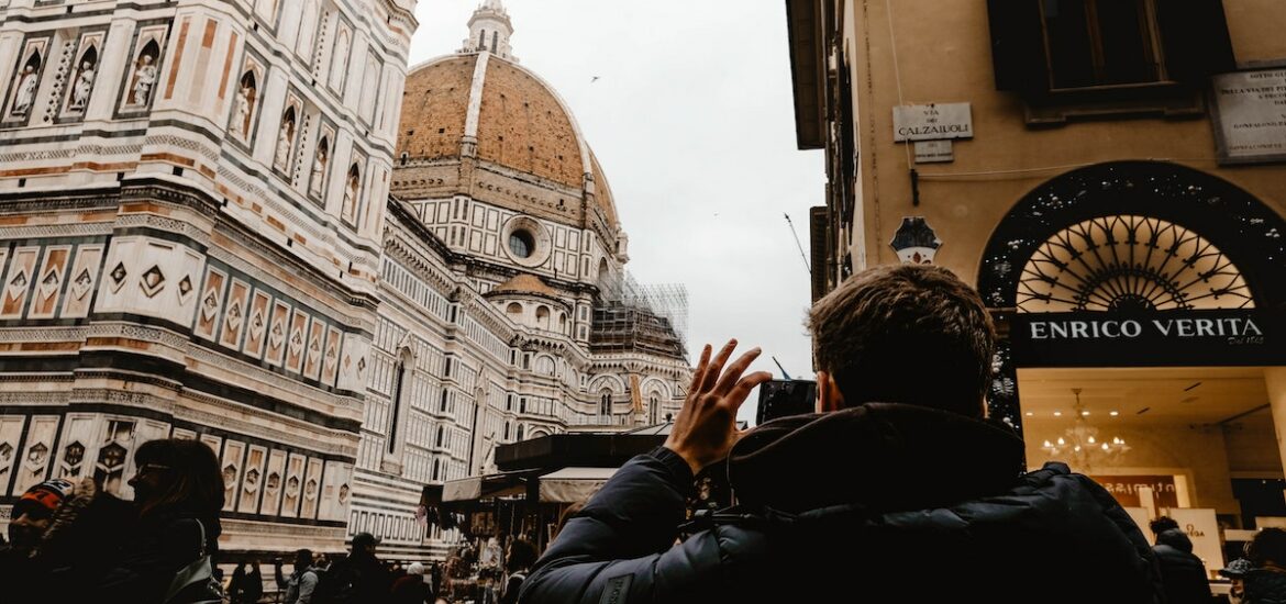 A man in a black winter coat taking a photo of Florence, Italy's red cathedral dome