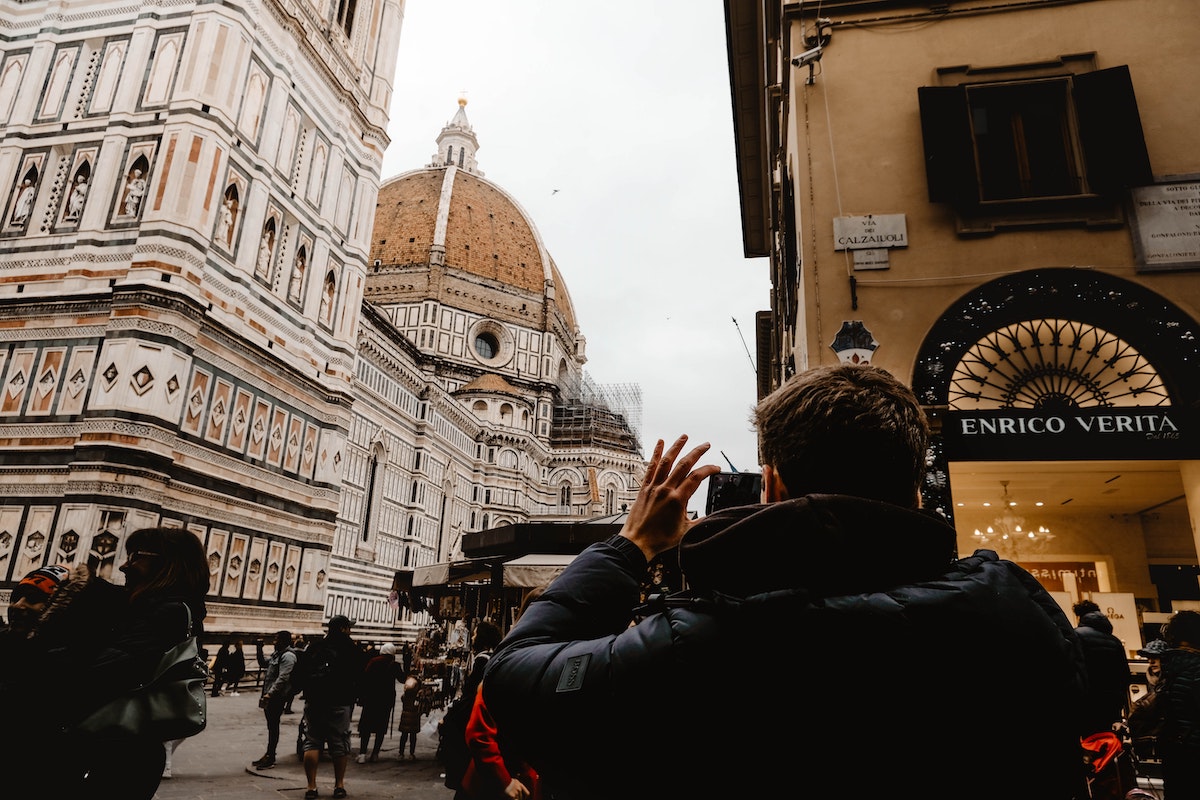 A man in a black winter coat taking a photo of Florence, Italy's red cathedral dome
