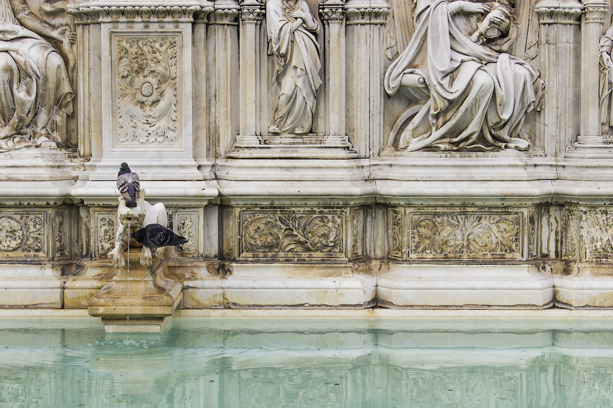 Intricately carved marble fountain with birds perched on one of its ledges