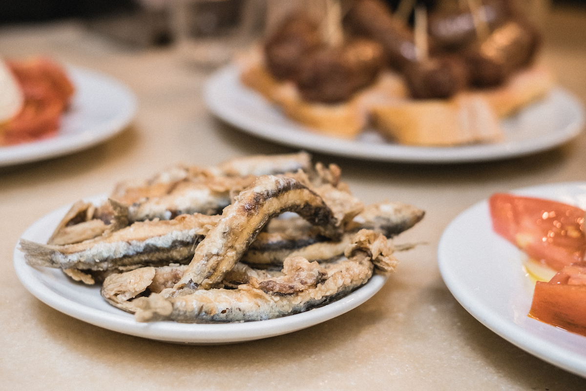 Close up of a plate of fried anchovies with several other dishes in the background.