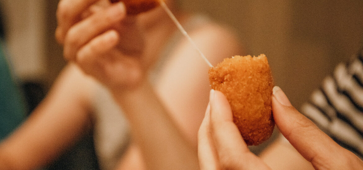A person breaking a fried croquette in half to release a string of melted cheese.
