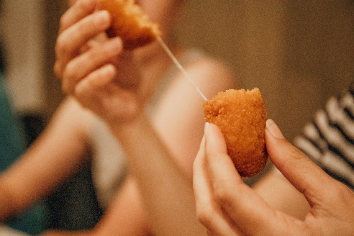 A person breaking a fried croquette in half to release a string of melted cheese.