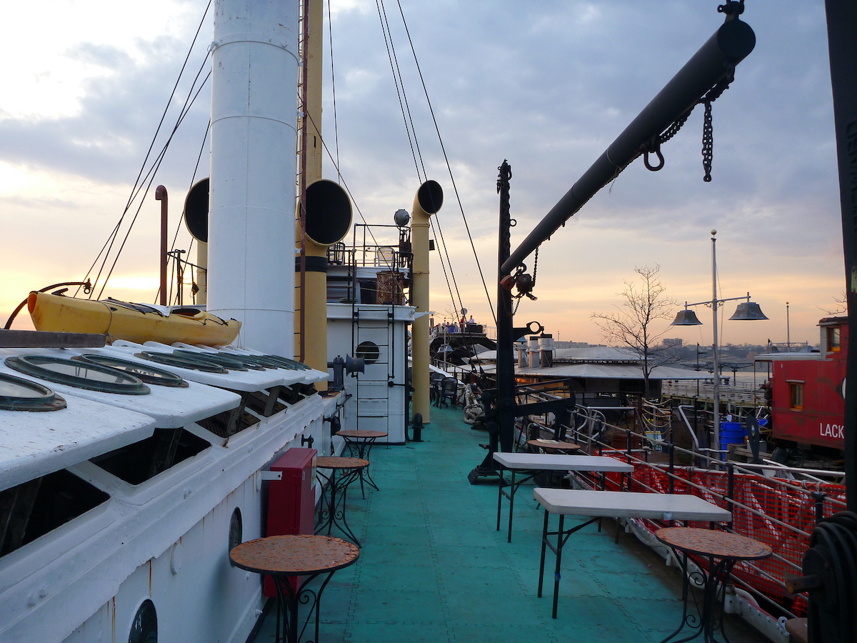 Small dining tables and chairs set up on the deck of a ship.